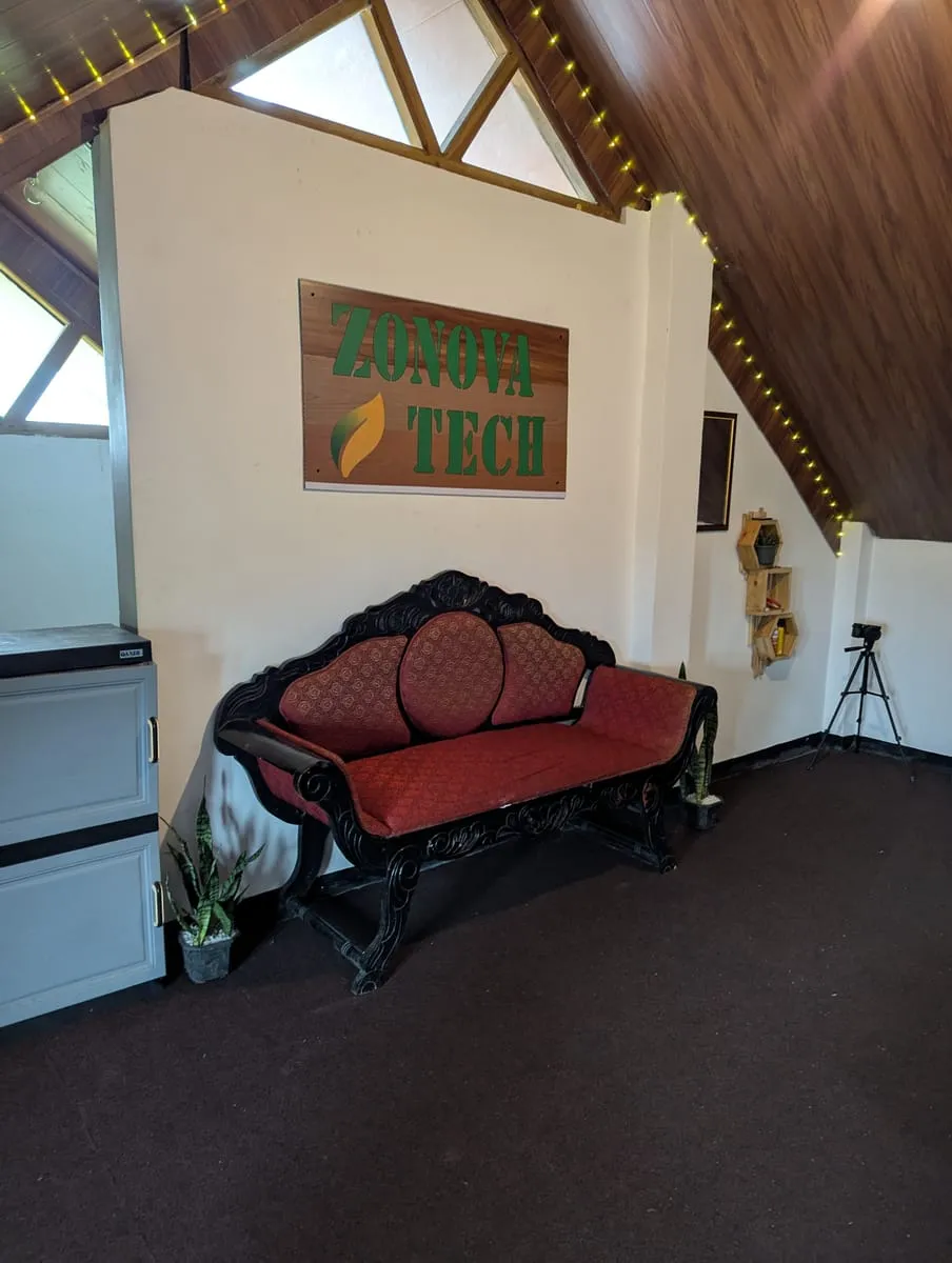 An antique carved sofa beneath Zonova Tech's hand-painted wooden sign, under an A-frame wooden ceiling strung with fairy lights.